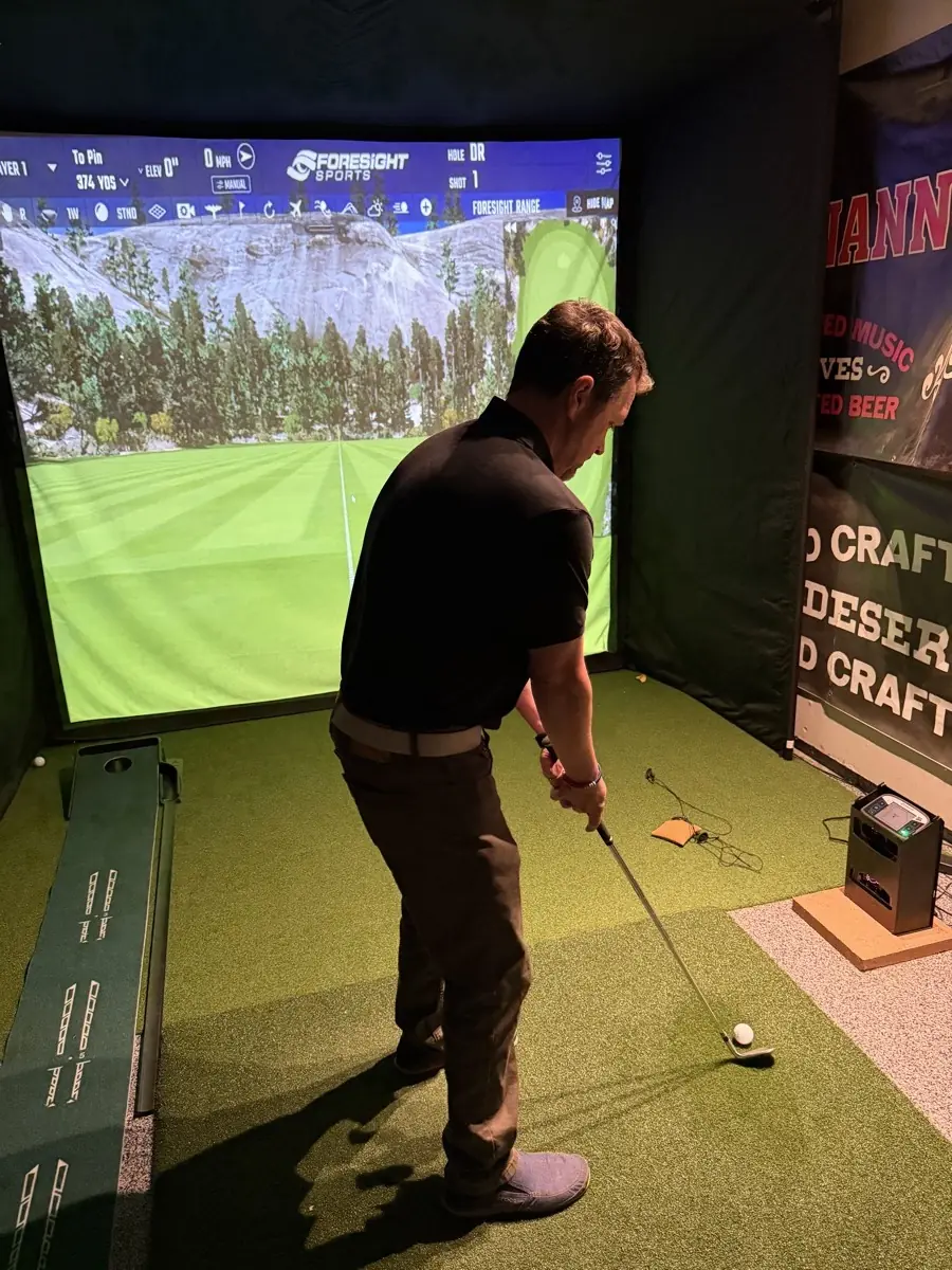 Kyle in a black shirt stepping onto the hitting mat in the simulator bay, with the GCQuad unit beside the mat and the screen behind