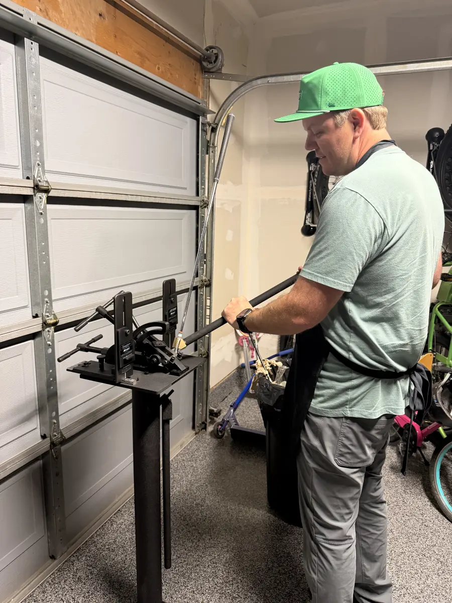 Kyle in his garage bending a golf club in the loft and lie machine, with the club clamped in the stand in front of him